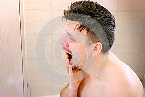 Portrait sleepy young man yawning and looking at mirror in bathroom in morning.