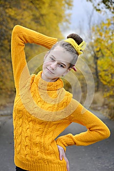 Portrait of a slender young girl in a yellow pullover against a background of autumn foliage