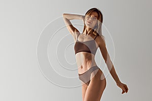 Portrait of slim, beautiful young woman in brown lingerie posing showing her perfect body shapes against grey studio