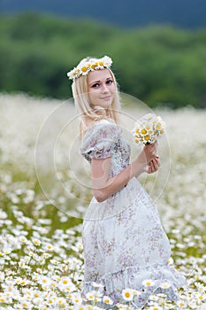 Portrait of slim girl in light dress against a chamomile field