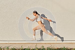 Portrait of slim sporty female wearing white top and beige leggins running over in the air, having energy, work out  on