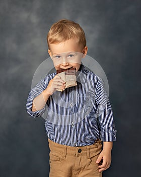 Portrait of small boy kid eating chocolate on grey background. Happy childhood concept. Sweet tooth.