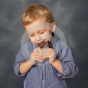 Portrait of small boy kid eating chocolate on grey background. Happy childhood concept. Sweet tooth.