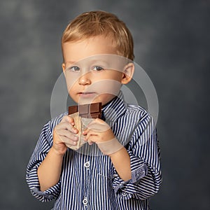 Portrait of small boy kid eating chocolate on grey background. Happy childhood concept. Sweet tooth.