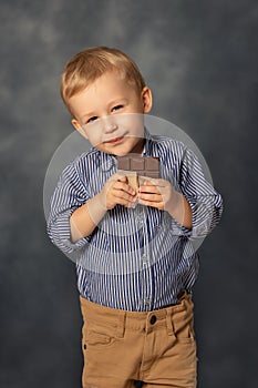 Portrait of small boy kid eating chocolate on grey background. Happy childhood concept. Sweet tooth.