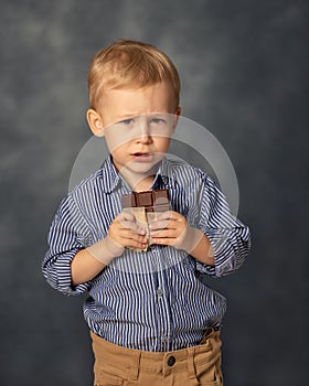 Portrait of small boy kid eating chocolate on grey background. Happy childhood concept. Sweet tooth.