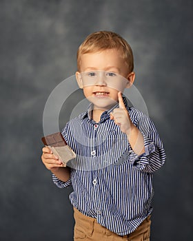 Portrait of small boy kid eating chocolate on grey background. Happy childhood concept. Sweet tooth.