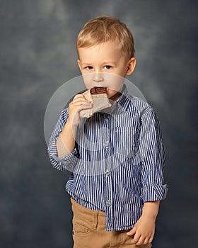 Portrait of small boy kid eating chocolate on grey background. Happy childhood concept. Sweet tooth.