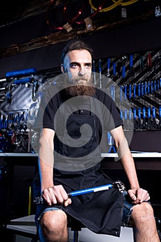 Portrait of small business owner of young man with beard. Guy bicycle mechanic workshop worker sitting with tool in his hand in a