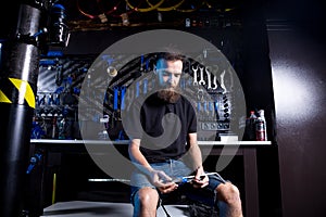 Portrait of small business owner of young man with beard. Guy bicycle mechanic workshop worker sitting with tool in his hand in a