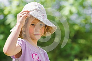 Portrait of a small caucasian girl with a hat protecting from the harsh sun. Green blur background.