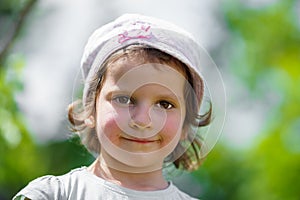 Portrait of a small caucasian girl with a hat protecting from the harsh sun. Green blur background.