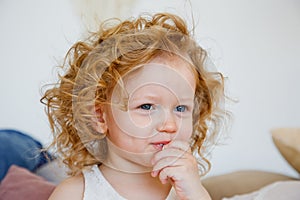 Portrait of a small curly-haired blonde girl during a meal. He eats something with his hands