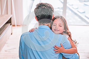 Portrait of small daughter with closed eyes hugging daddy at home