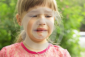 Portrait of a small, fair-haired girl who is crying in the open air