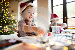 Portrait of small girl and boy indoors at home at Christmas, painting pictures.