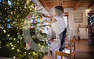 Portrait of small girl indoors at home at Christmas, decorating tree.