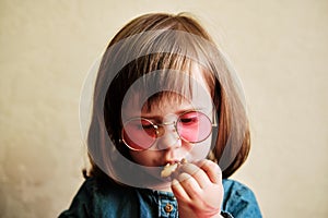 Portrait of a small girl in pink glasses. A toddler eating cookings at home