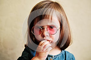 Portrait of a small girl in pink glasses. A toddler eating cookings at home