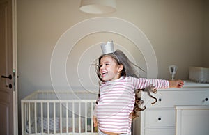 Portrait of small girl with princess crown on head indoors, having fun.