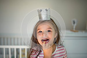 Portrait of small girl with princess crown on head indoors, looking at camera.