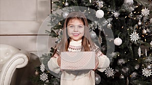 Portrait of a small and happy girl who is holding a box with a Christmas present and giving it