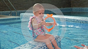 Portrait of a small one-year-old girl in the pool, she sits on the edge of pool.