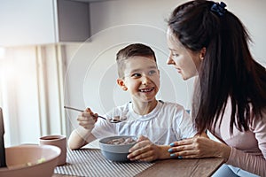 Portrait, small teen boy eating cereals with milk in kichen and looking at mother with smile.