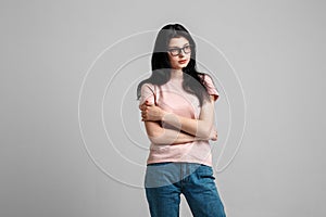 Portrait of smart beautiful brunette girl in eyeglasses with natural make-up, on grey background.