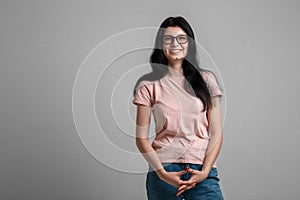 Portrait of smart beautiful brunette girl in eyeglasses with natural make-up, on grey background.