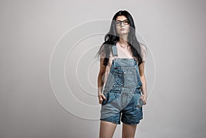 Portrait of smart beautiful brunette girl in eyeglasses with natural make-up, on grey background.