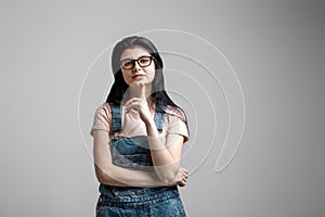 Portrait of smart beautiful brunette girl in eyeglasses with natural make-up, on grey background.