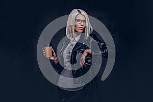 Portrait of a smart blonde female photographer in trendy clothes and glasses holds a takeaway coffee and posing while