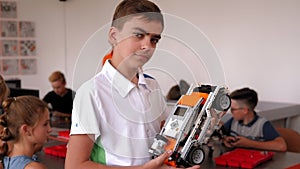 Portrait of a smart boy in a robotics class at school, holding a robot.