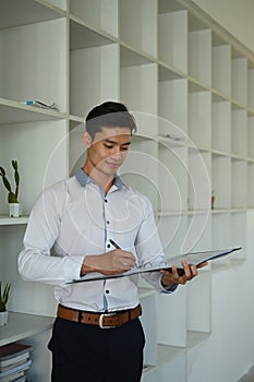 Portrait of smart businessman checking financial reports while standing near bookshelf at modern office