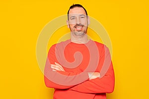 Portrait of a smart, cheerful and attractive bearded Hispanic man in his 40s, arms crossed, isolated over yellow colored