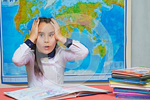 Portrait of a smart cute girl holding her head against the background of the world map. The inscription on the map WORLD
