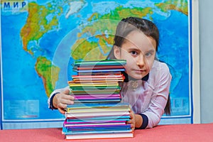 Portrait of a smart cute girl hugging a lot of books on the background of the world map