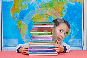 Portrait of a smart cute girl hugging a lot of books on the background of the world map