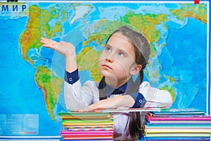 Portrait of a smart cute girl hugging a lot of books on the background of the world map