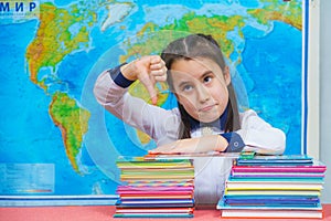 Portrait of a smart cute girl hugging a lot of books on the background of the world map. Thumbs down