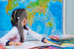 Portrait of a smart cute girl reading books on the background of the world map.