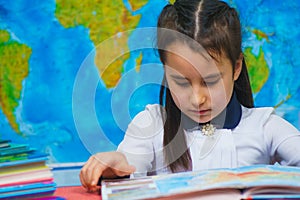 Portrait of a smart cute girl reading books on the background of the world map.