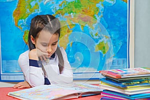 Portrait of a smart cute girl reading books on the background of the world map.