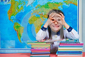 Portrait of a smart cute girl reading books on the background of the world map. Shows glasses with his hands