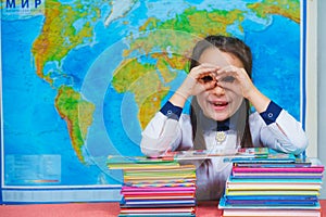 Portrait of a smart cute girl reading books on the background of the world map. Shows glasses with his hands