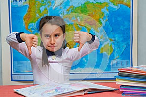 Portrait of a smart cute girl showing thumbs down on the background of the world map