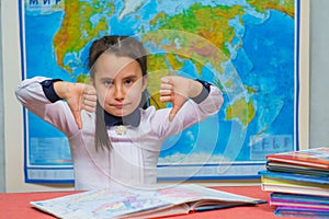 Portrait of a smart cute girl showing thumbs down on the background of the world map. The inscription on the map WORLD