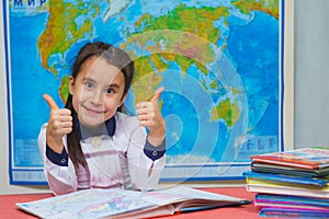 Portrait of a smart cute girl showing thumbs up on the background of the world map. The inscription on the map WORLD