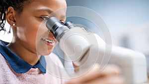 Portrait of Smart Little Schoolgirl Looking Under the Microscope. In Elementary School